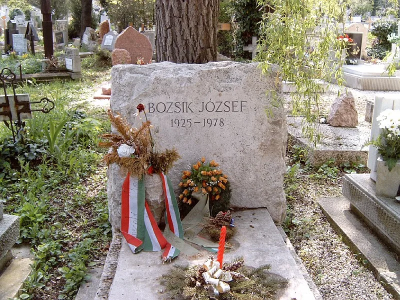 나무 그늘 아래 BOZSIK JÓZSEF 1925-1978이 새겨진 돌 묘비와 헝가리 삼색 리본이 달린 화환