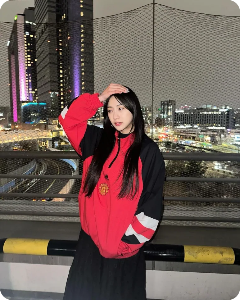 도시의 야경을 배경으로 맨유 검정·빨강 셸 파카를 입은 오하영