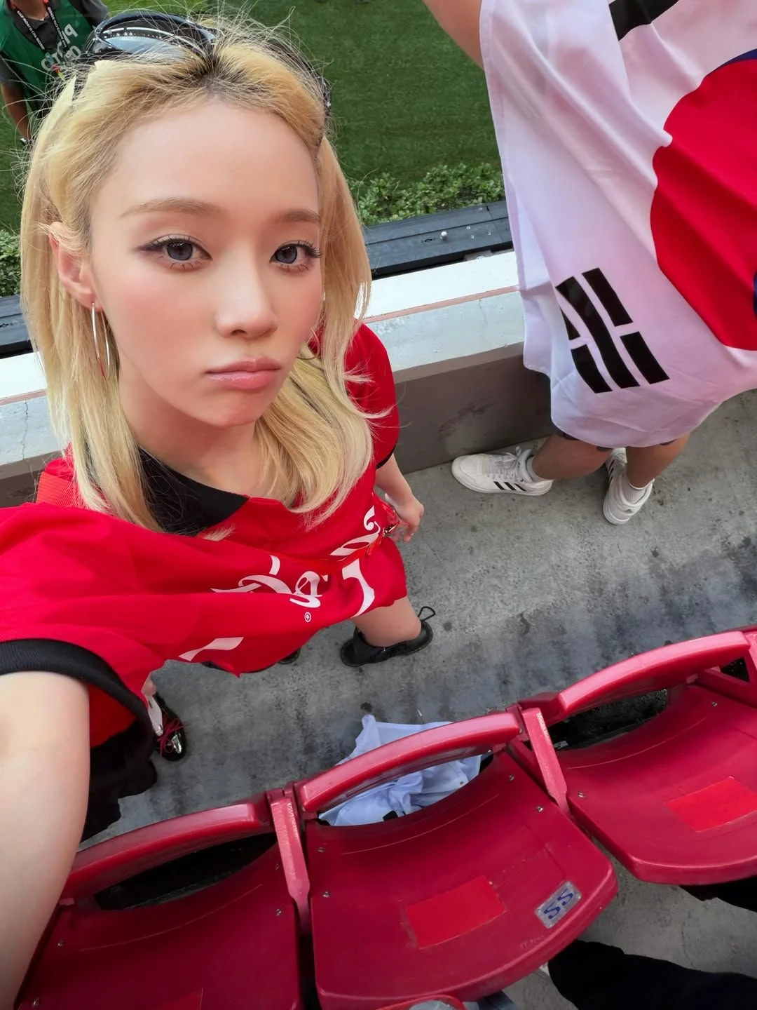 빨간 코카콜라 축구 저지와 검은 롱부츠를 신고 태극기를 든 윈터의 경기장 셀피